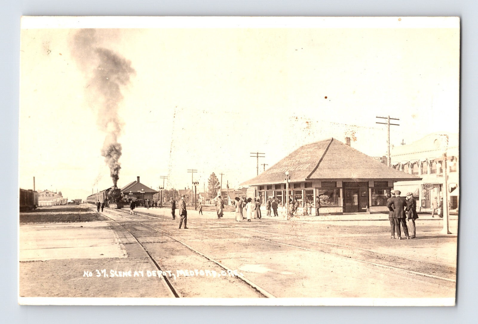 Vintage black and white photo of a street scene with people and a steam train, likely from the early 20th century.