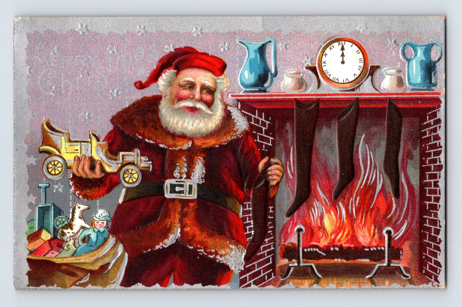 Santa Claus beside fireplace holding toy automobile with stockings, toys, and burning hearth on embossed vintage Christmas postcard.