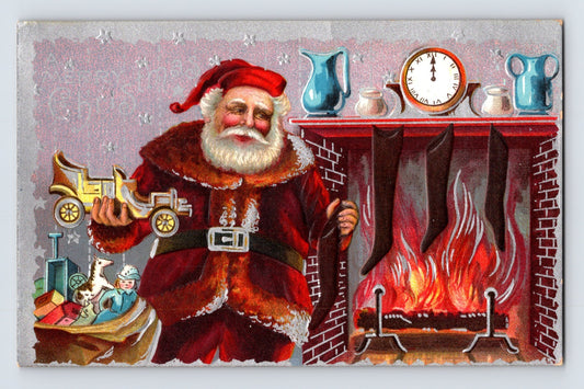 Santa Claus beside fireplace holding toy automobile with stockings, toys, and burning hearth on embossed vintage Christmas postcard.