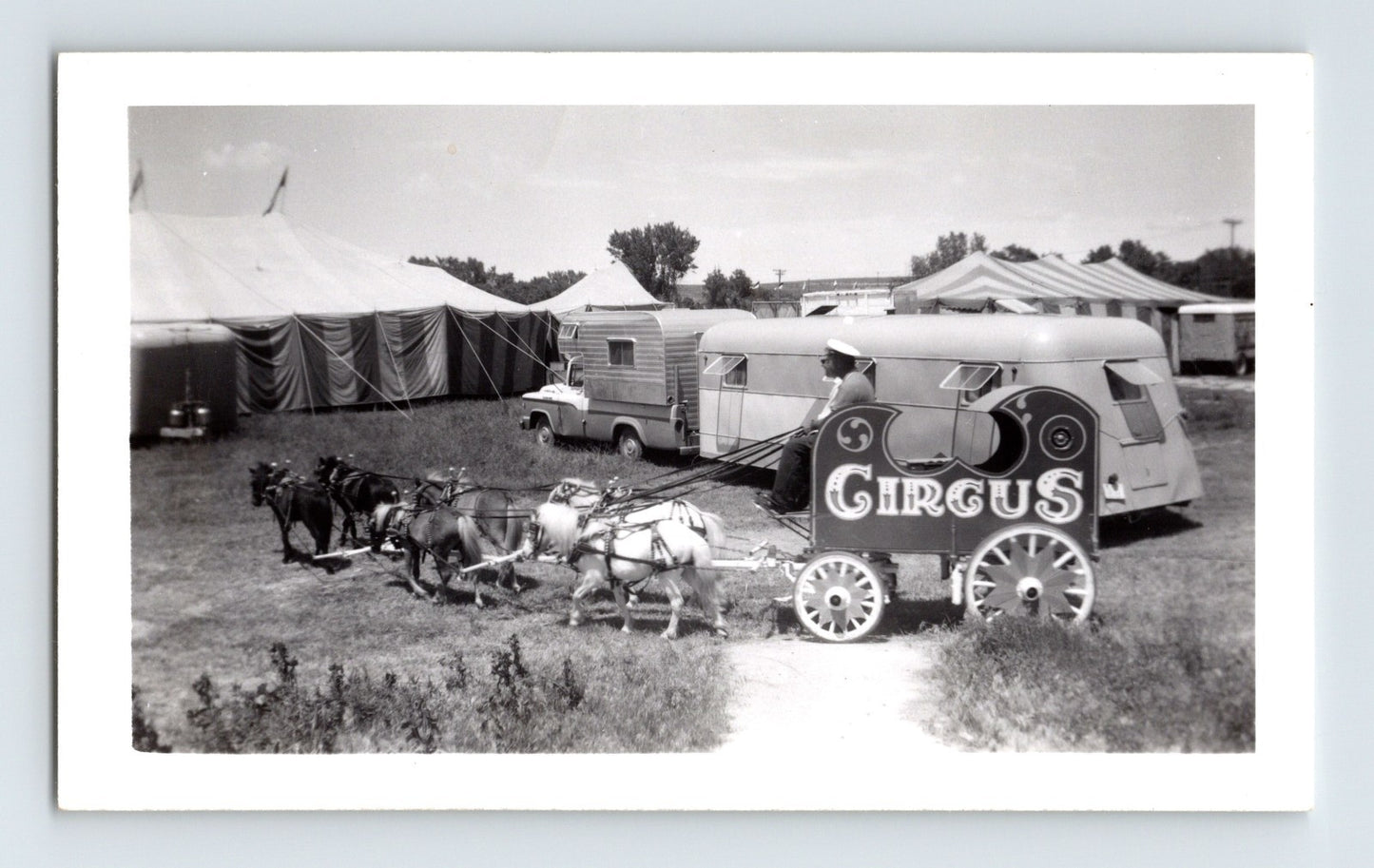 1962 black and white photograph of Fairyland Circus miniature horse-drawn wagon with circus sign, small trailer, and striped tents in background