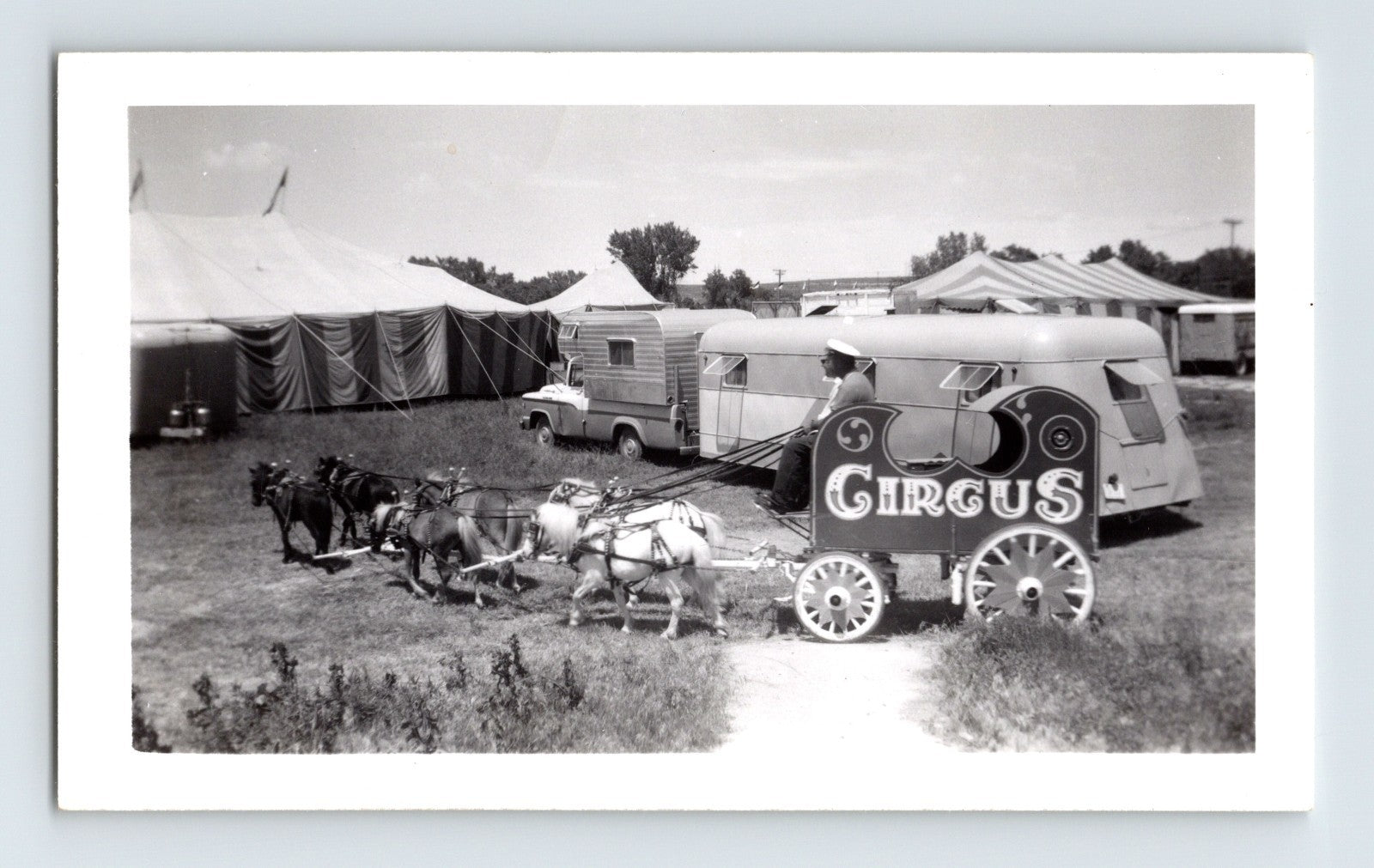1962 black and white photograph of Fairyland Circus miniature horse-drawn wagon with circus sign, small trailer, and striped tents in background