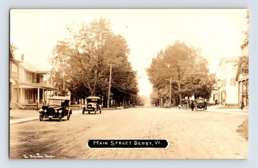 Derby Vermont Main Street real photo postcard with early automobiles, dirt roadway, and downtown buildings during the 1920s.