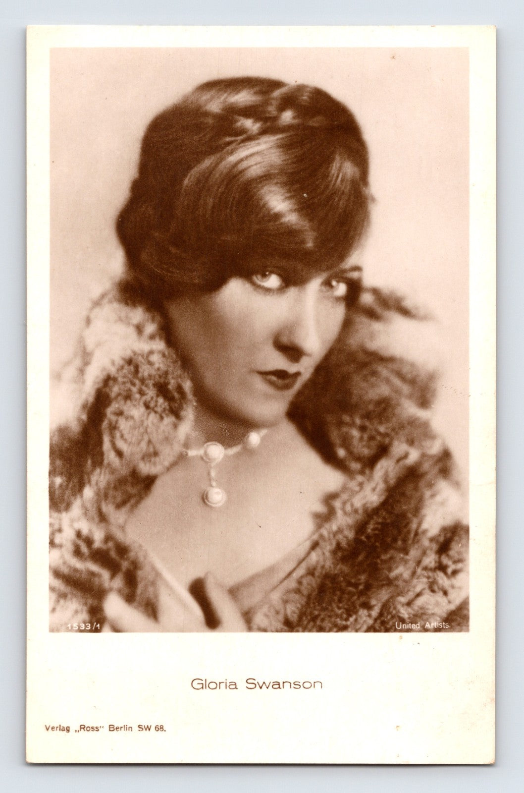 Real photo postcard portrait of Gloria Swanson wearing fur wrap and necklace in 1930s studio publicity image