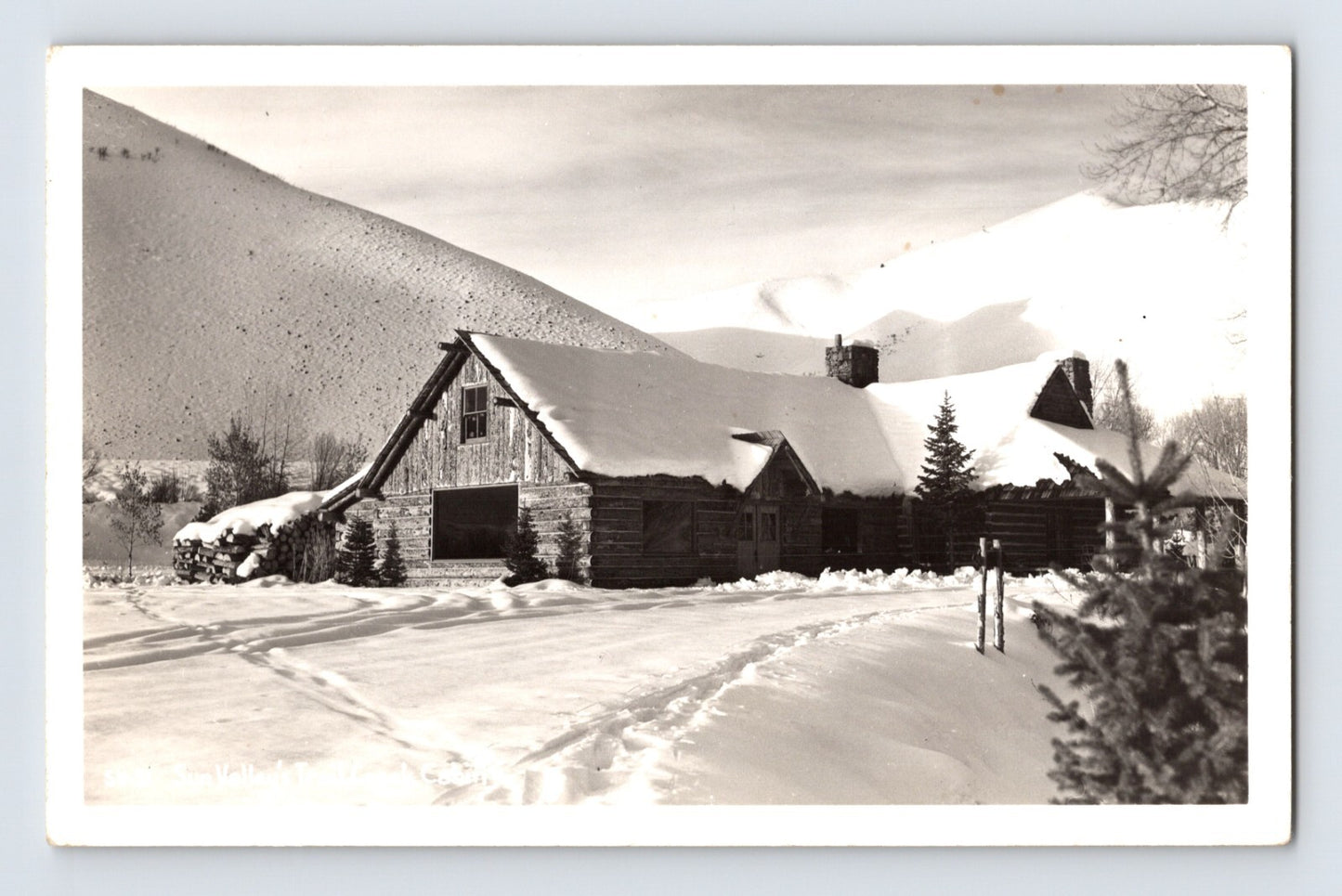 Sun Valley Idaho Trail Creek Cabin in winter snow with log lodge buildings and mountain slope background real photo postcard