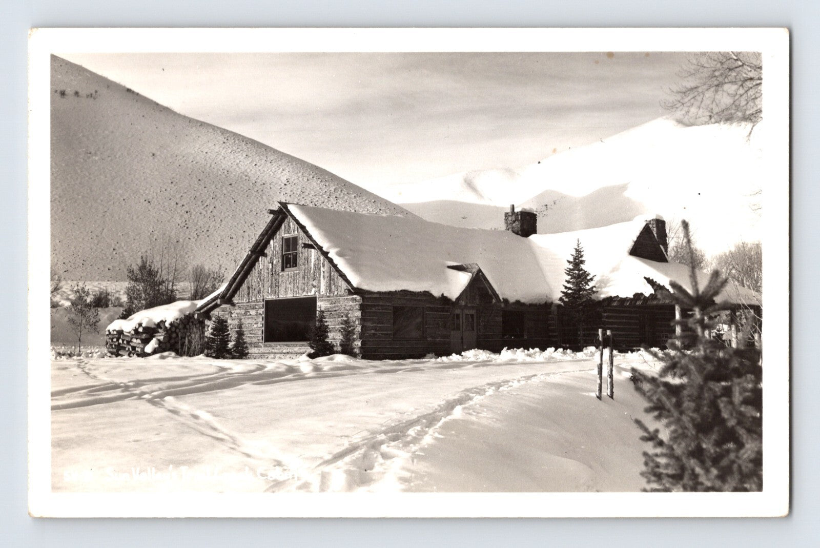 Sun Valley Idaho Trail Creek Cabin in winter snow with log lodge buildings and mountain slope background real photo postcard