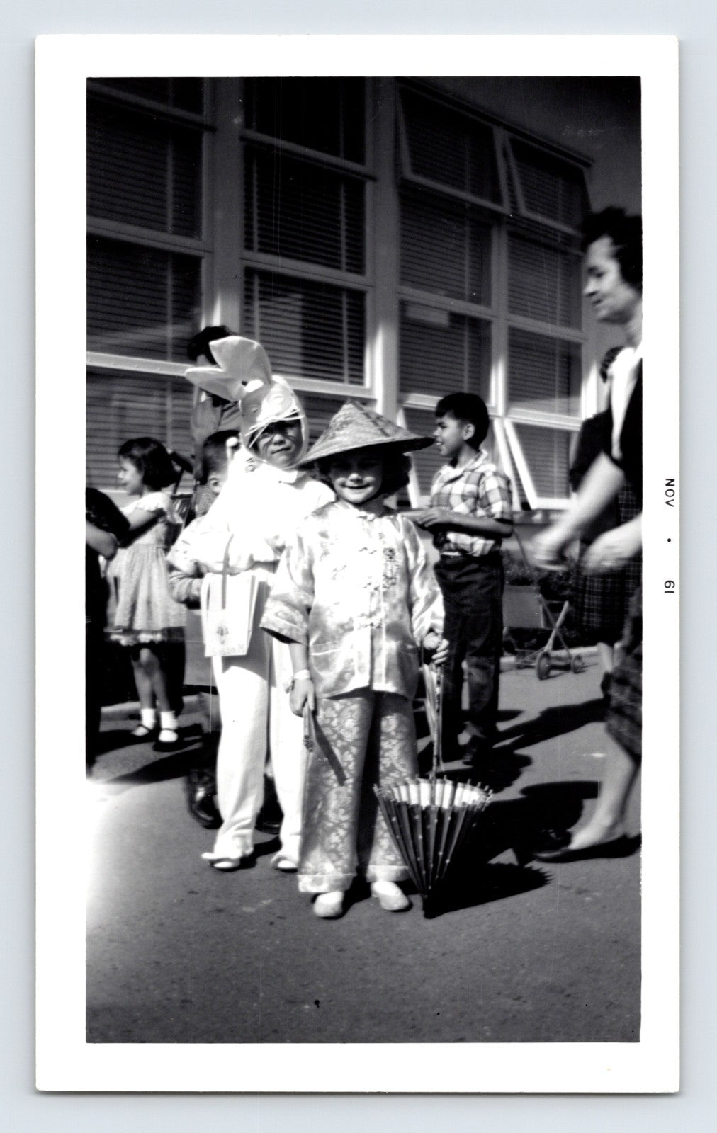 Children in costume parade schoolyard Halloween outfits rabbit and Asian costume umbrella 1960s snapshot