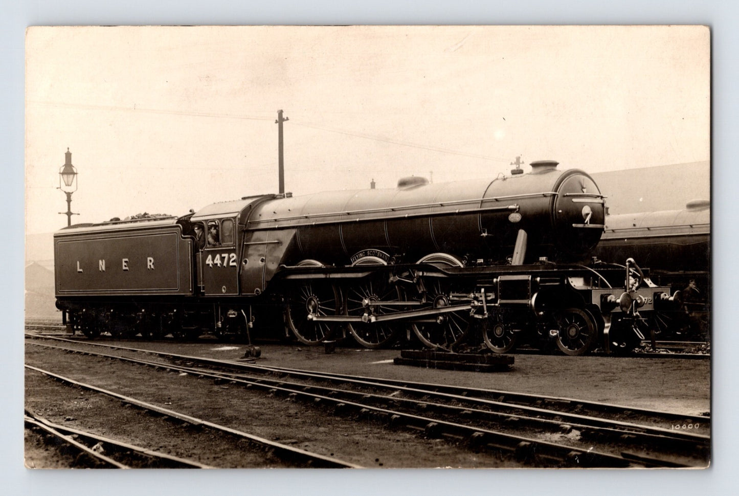 1910s postcard showing a London and North Eastern Railway steam locomotive identified as the Flying Scotsman beside rail yard tracks and station infrastructure.