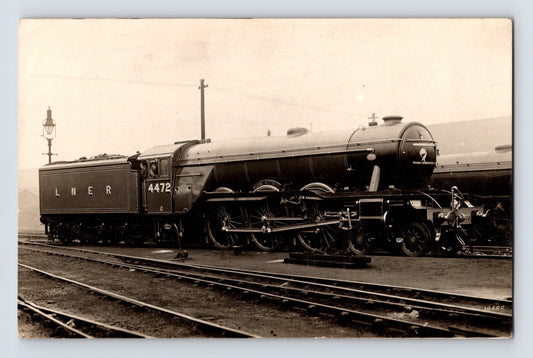 1910s postcard showing a London and North Eastern Railway steam locomotive identified as the Flying Scotsman beside rail yard tracks and station infrastructure.