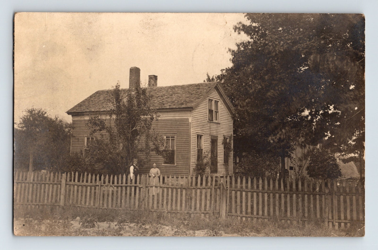 Real photo postcard of a wood frame residence with picket fence and two figures in yard Butler Pennsylvania circa 1910