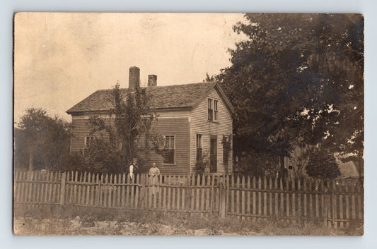 Real photo postcard of a wood frame residence with picket fence and two figures in yard Butler Pennsylvania circa 1910