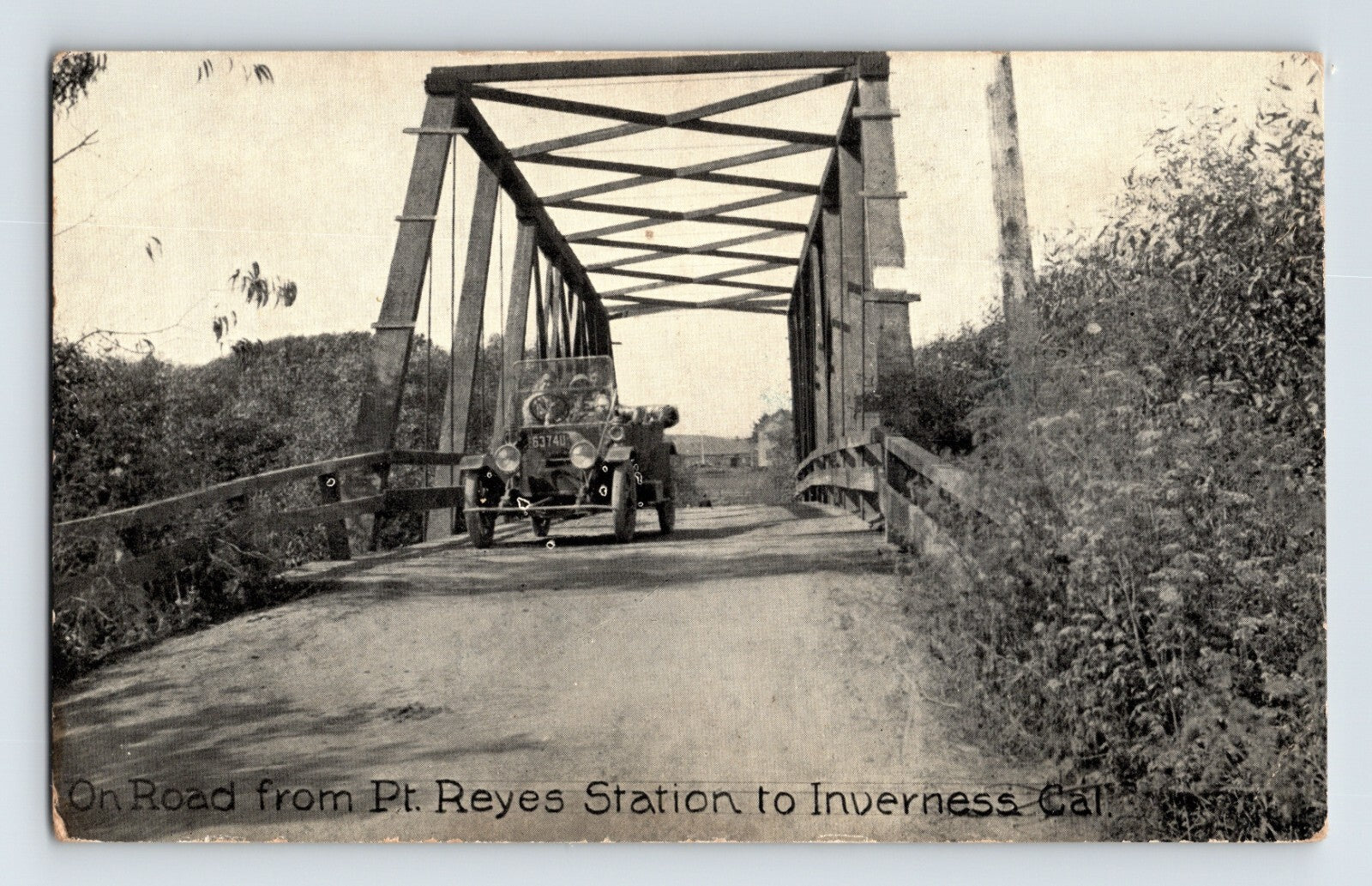 Vintage postcard of a car crossing a bridge with text indicating the route from Pt Reyes Station to Inverness, California.