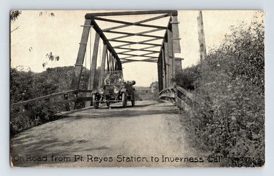 Vintage postcard of a car crossing a bridge with text indicating the route from Pt Reyes Station to Inverness, California.