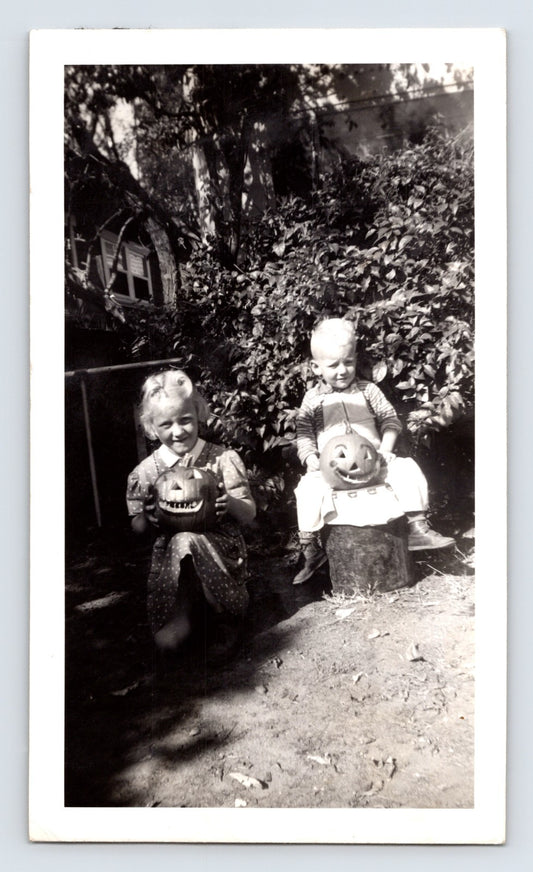 Two children holding carved pumpkins jack o lanterns backyard Halloween snapshot mid century