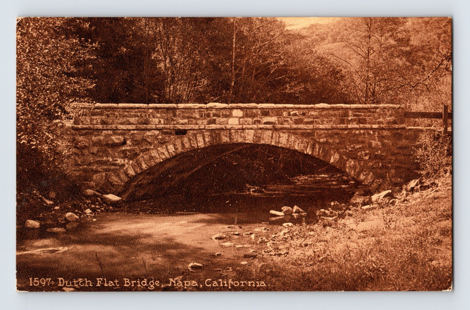 Napa California Dutch Flat Bridge postcard showing rustic stone arch bridge crossing a wooded creek in sepia photographic tones.