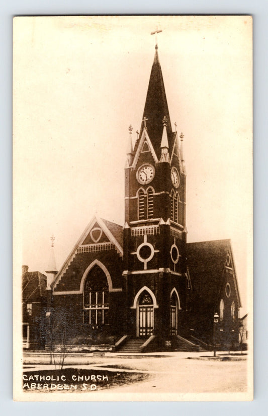 Catholic Church in Aberdeen South Dakota with tall Gothic Revival clock tower and pointed spire, early twentieth century real photo postcard view