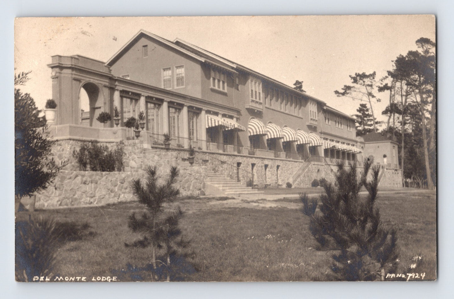 Sepia-tone real photo postcard of the Del Monte Lodge at Pebble Beach, California, showing the large resort building with terraces, striped awnings, and landscaped grounds.