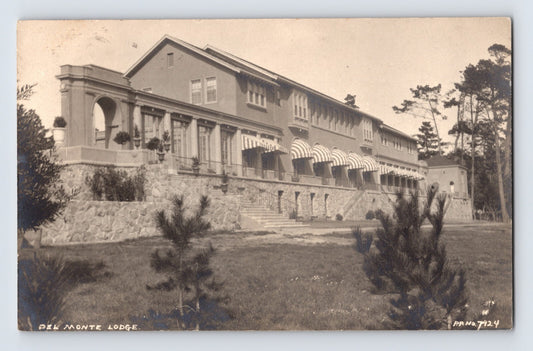 Sepia-tone real photo postcard of the Del Monte Lodge at Pebble Beach, California, showing the large resort building with terraces, striped awnings, and landscaped grounds.