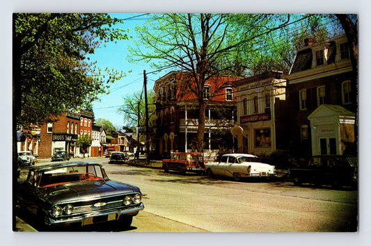 1960s postcard showing Main Street in downtown Fishkill, New York, with period storefronts, parked cars including a Chevrolet Impala, and tree-lined commercial buildings.