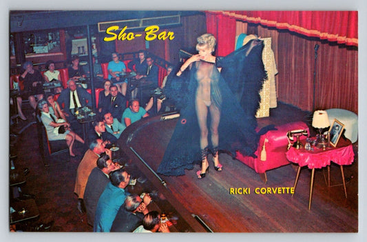 Ricki Corvette performing burlesque on stage at Sho Bar club in New Orleans with seated audience and red curtain backdrop