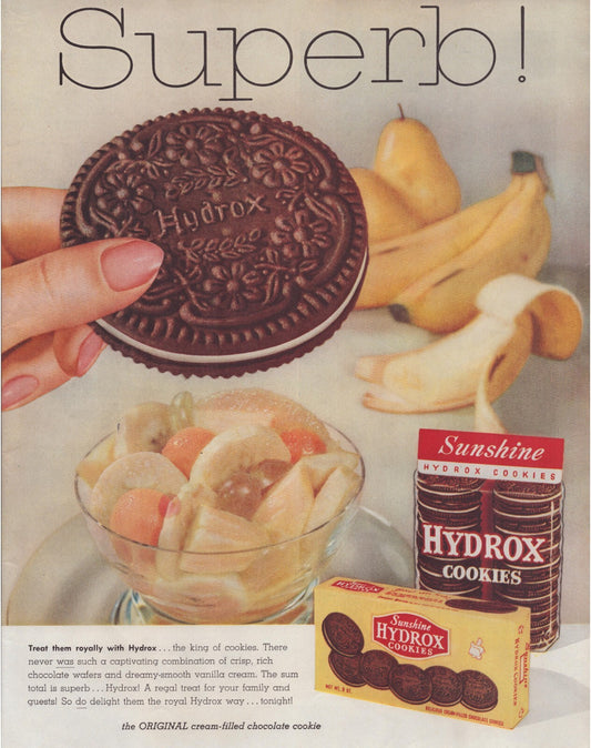 1957 Sunshine Hydrox cookies print ad featuring hand holding chocolate sandwich cookie with banana and fruit dessert background full page magazine ad