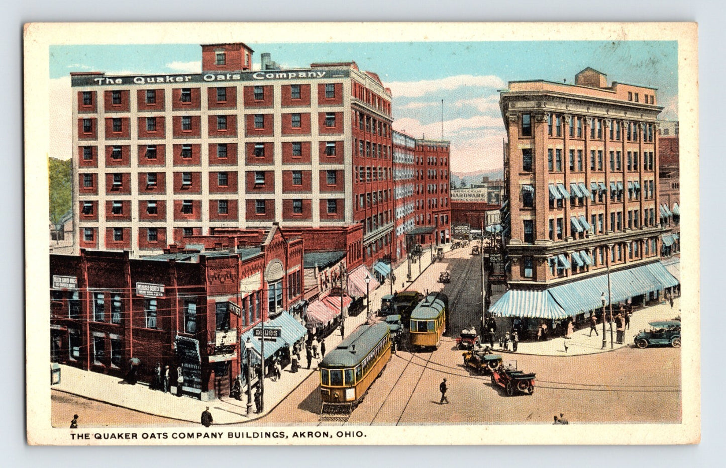 Colorized postcard view of downtown Akron, Ohio, featuring the Quaker Oats Company buildings, streetcars, automobiles, and busy commercial intersections.