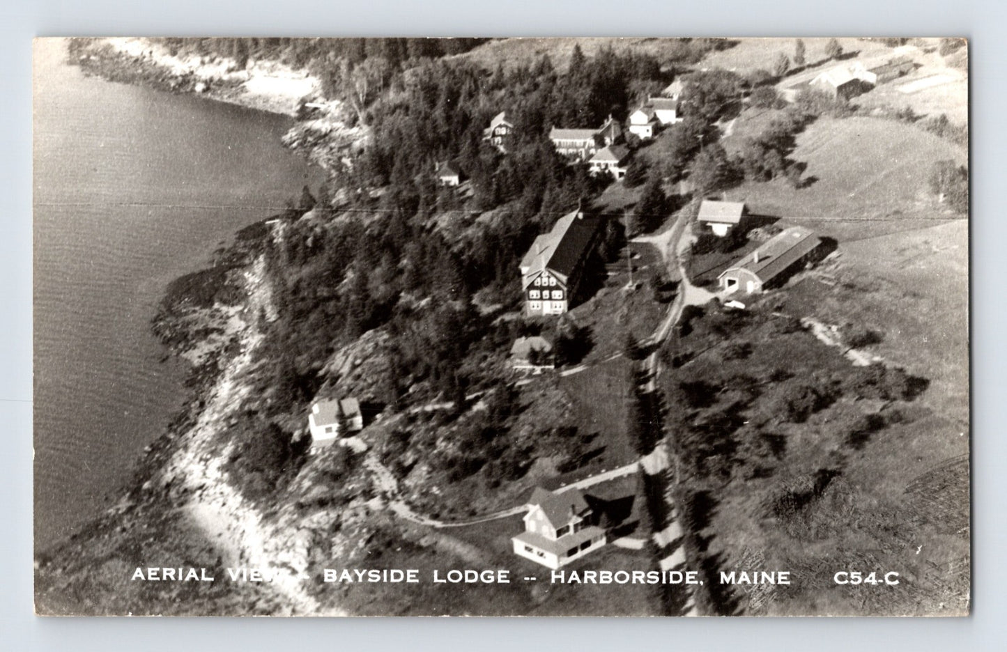 Harborside Maine Bayside Lodge aerial view showing waterfront buildings and wooded shoreline, 1950s real photo postcard
