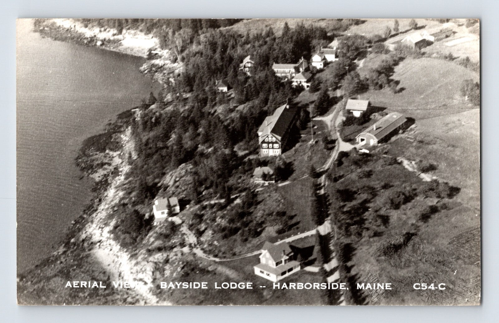 Harborside Maine Bayside Lodge aerial view showing waterfront buildings and wooded shoreline, 1950s real photo postcard