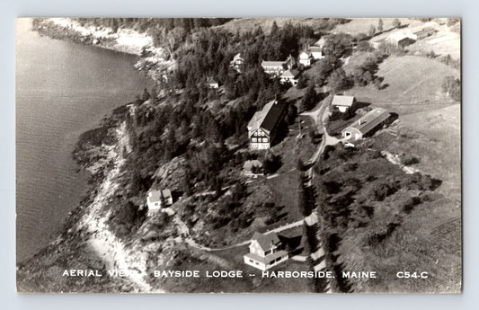 Harborside Maine Bayside Lodge aerial view showing waterfront buildings and wooded shoreline, 1950s real photo postcard