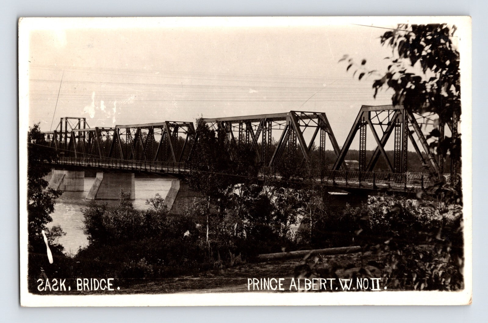 1911 Prince Albert Saskatchewan railroad bridge real photo postcard showing steel truss bridge spanning river with trees in foreground