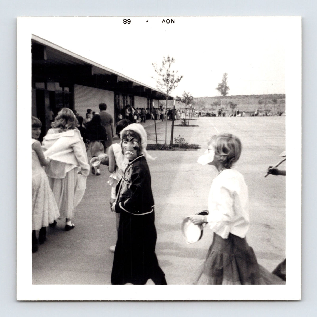 Halloween school parade child mask turning toward camera playground line costumes 1960s snapshot 3.5 x 3.5 photo