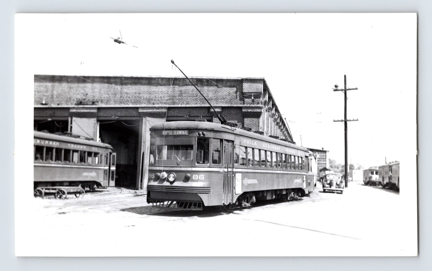 Philadelphia Suburban Transportation Company trolley car 86 at 69th Street Terminal, 1951, black and white photo with brick car barn and adjacent streetcars visible