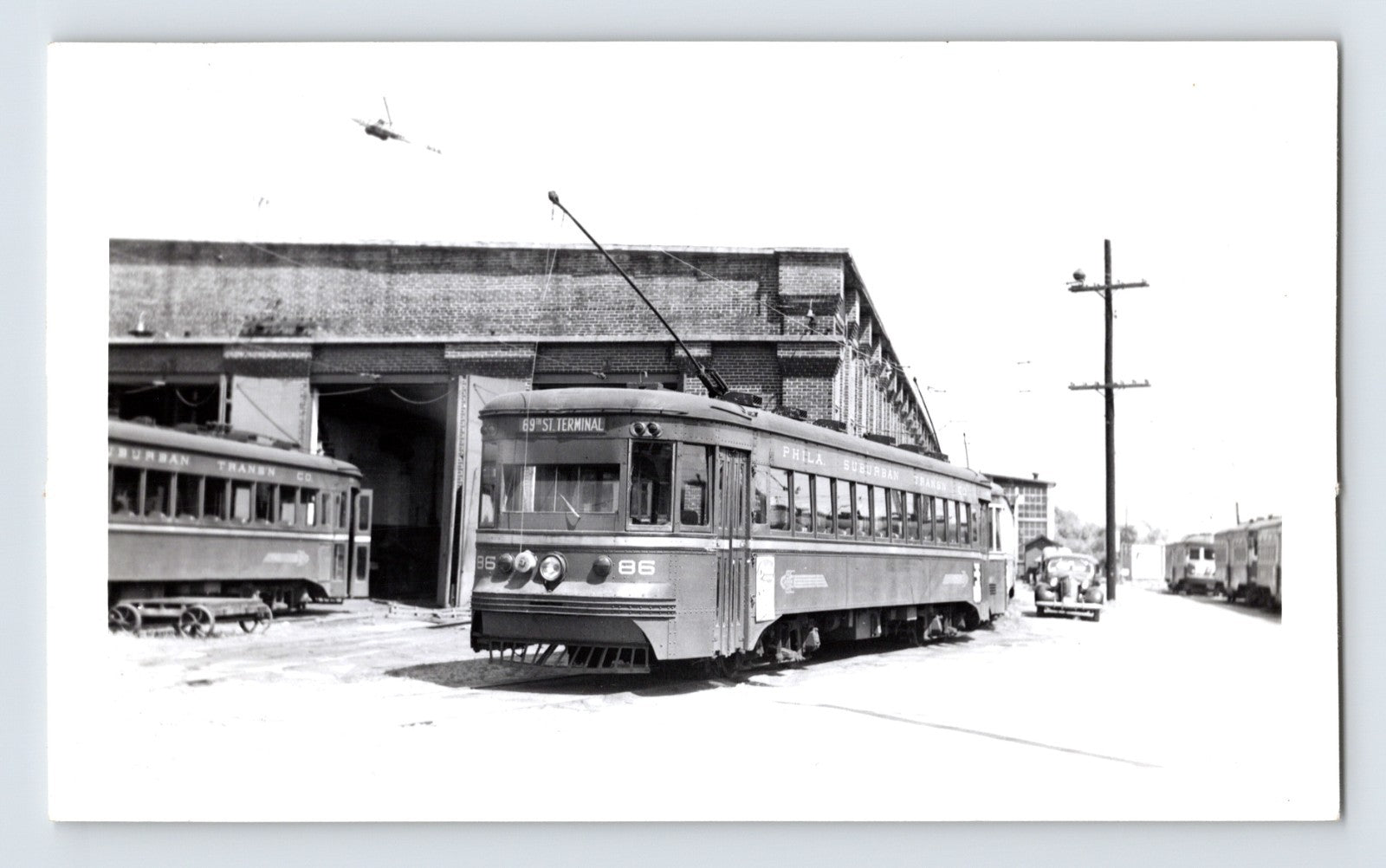 Philadelphia Suburban Transportation Company trolley car 86 at 69th Street Terminal, 1951, black and white photo with brick car barn and adjacent streetcars visible