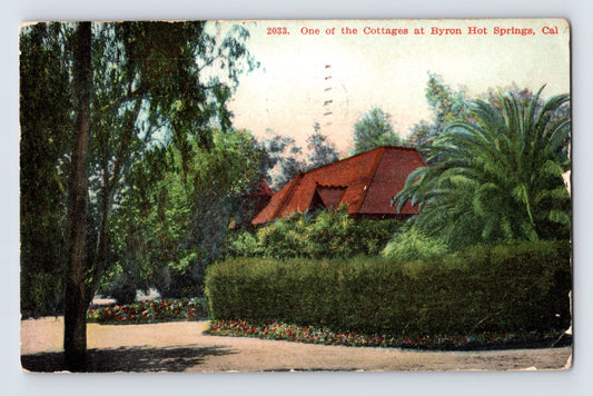 Byron Hot Springs California cottage postcard showing landscaped resort grounds with palm trees, hedges, and rustic bungalow-style lodging cottage.