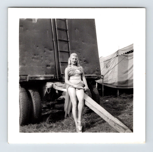Black and white photo of a woman sitting on a wooden ramp next to a trailer.