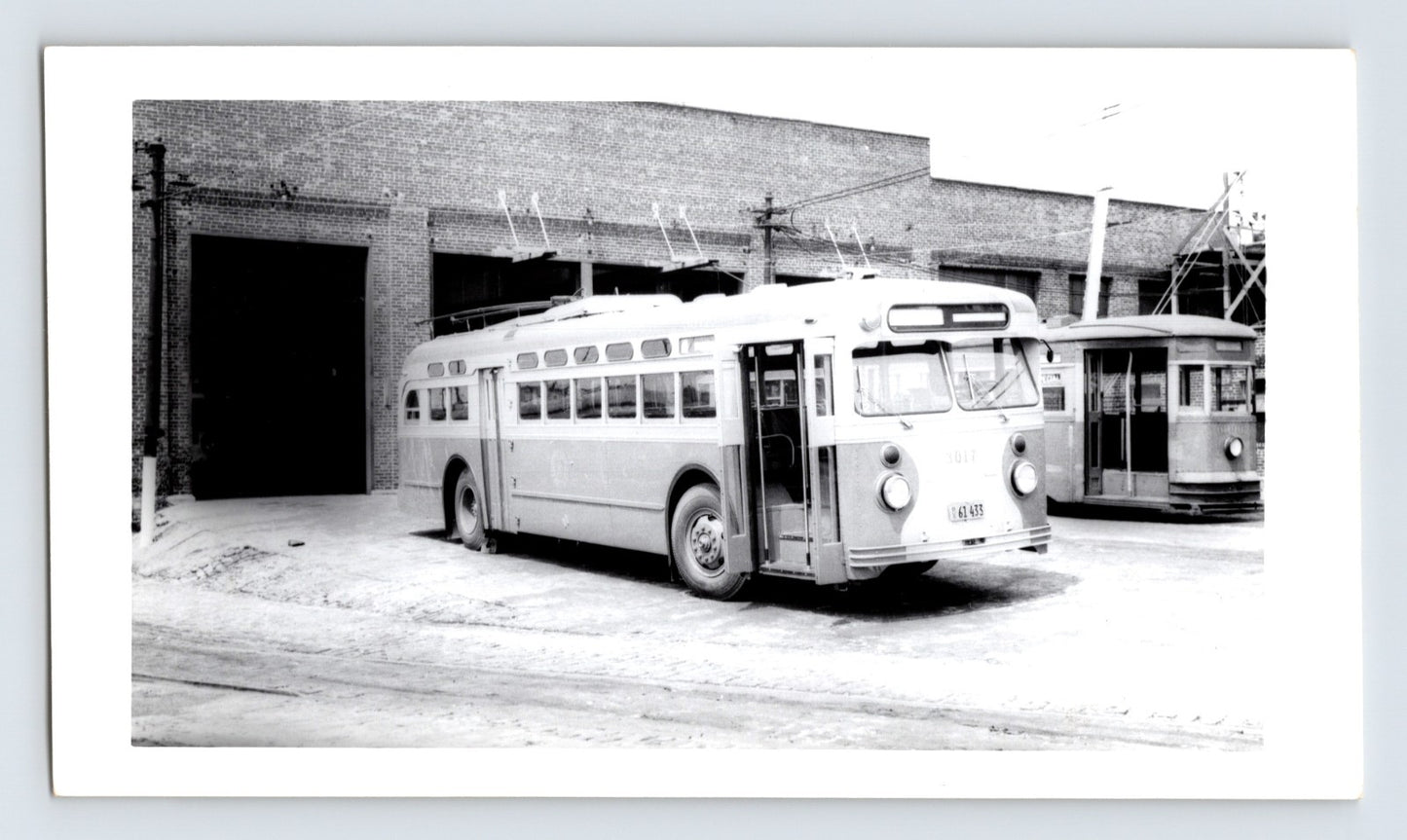 Chicago Transit Authority trolley coach 3017 at DeKalb Shops carhouse with overhead wires and brick garage bay, mid-century black and white transit photograph