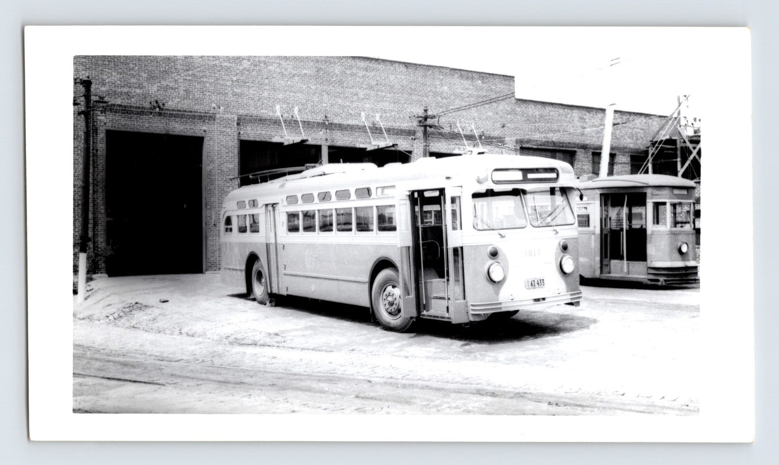 Chicago Transit Authority trolley coach 3017 at DeKalb Shops carhouse with overhead wires and brick garage bay, mid-century black and white transit photograph