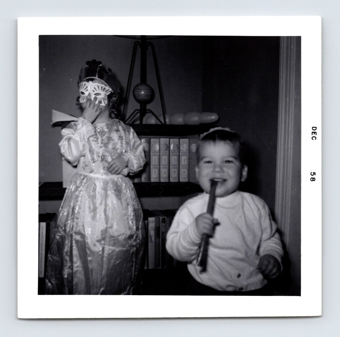 two children indoors one wearing mask costume other holding stick December 1958 black and white photo