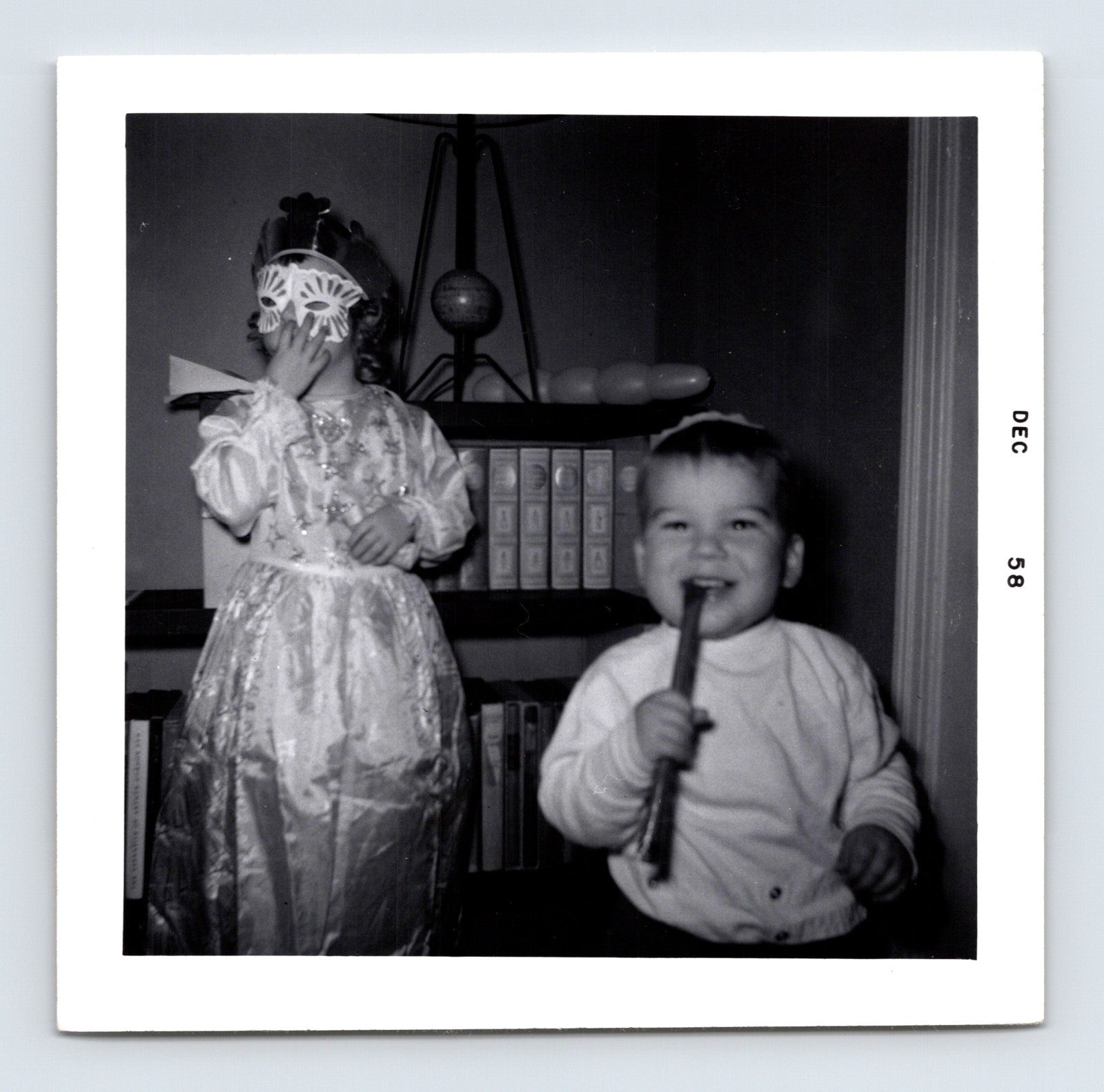 two children indoors one wearing mask costume other holding stick December 1958 black and white photo