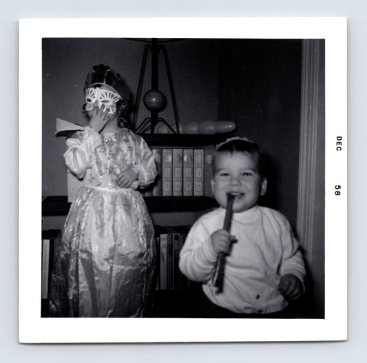 two children indoors one wearing mask costume other holding stick December 1958 black and white photo