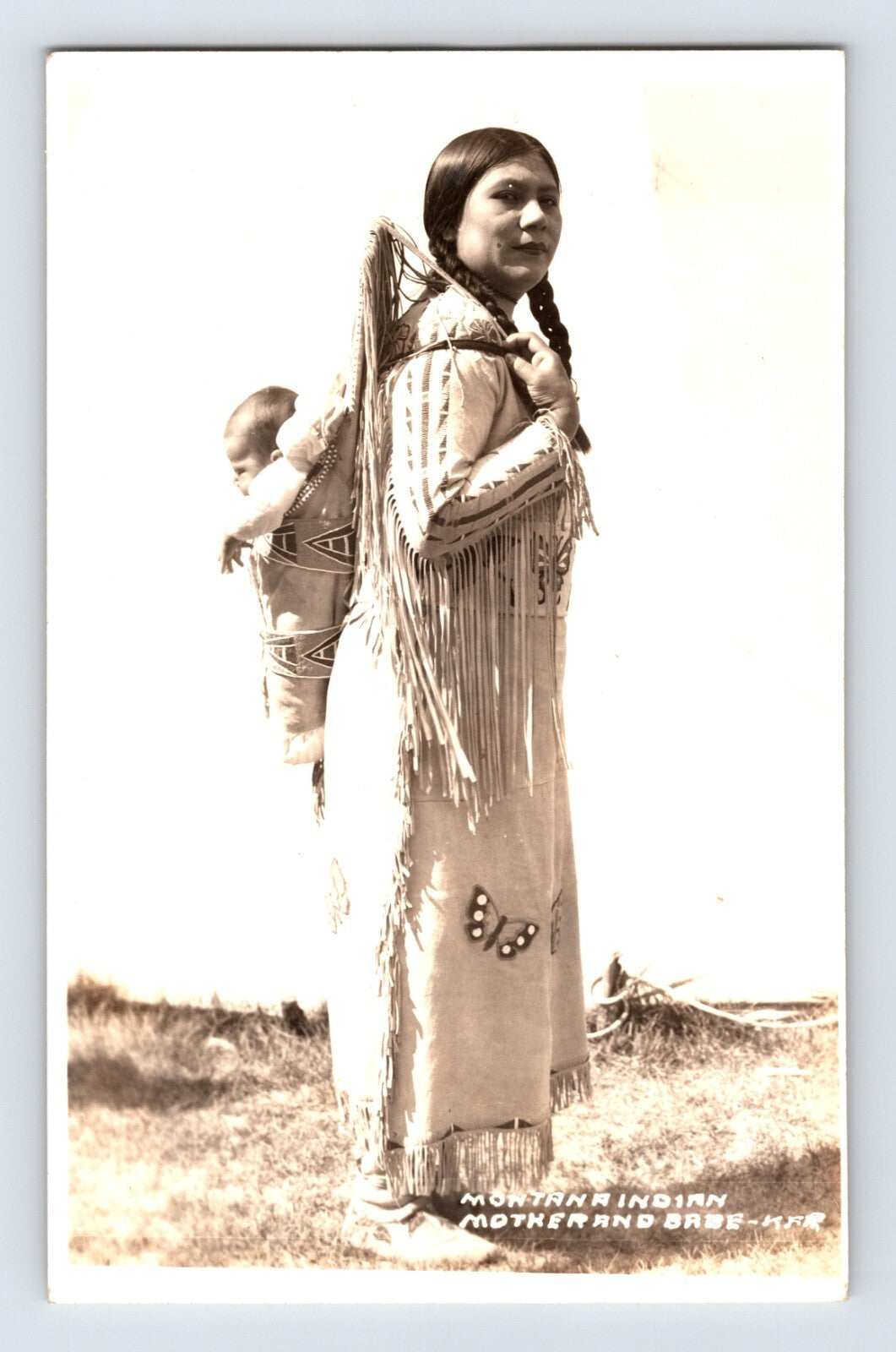Postcard front showing Native American woman carrying a child in cradleboard, studio captioned Montana Indian K. F. Roahan photo, 1940s