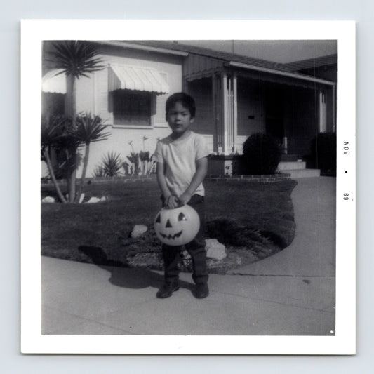 Halloween snapshot of young child holding jack o lantern trick or treat bucket in front of mid century suburban house daytime 3.5 x 3.5 photo