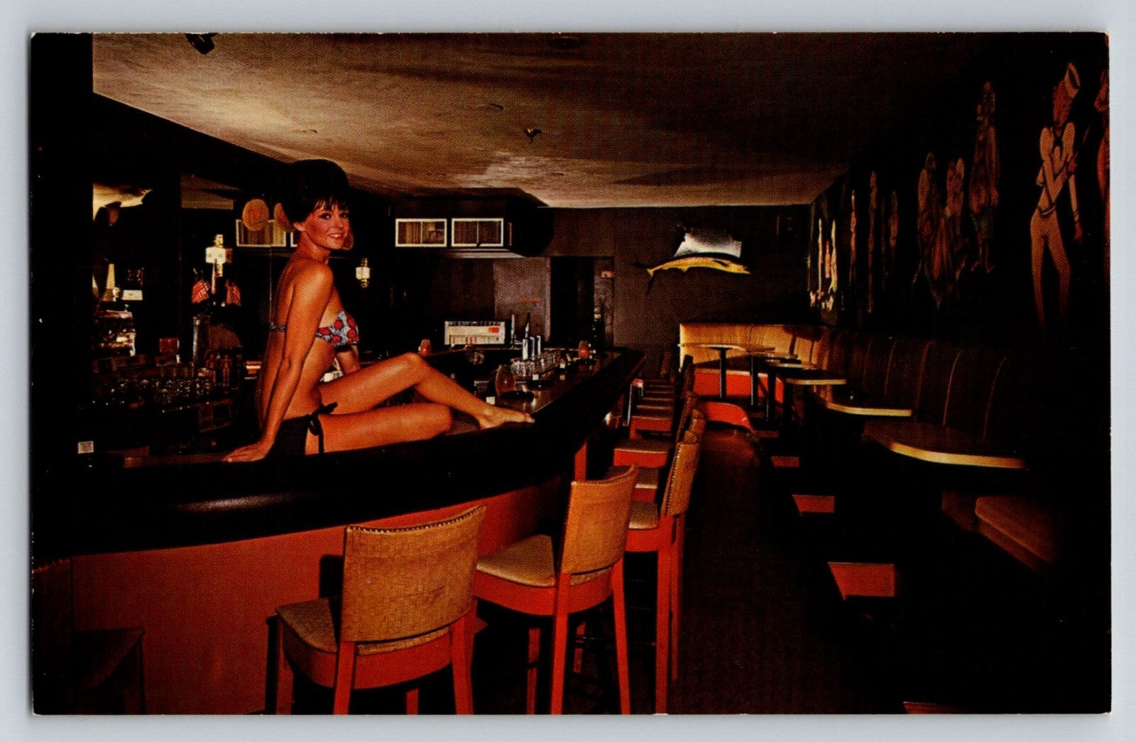 Color postcard of Bikini Lounge in Fort Lauderdale Florida showing woman seated on bar counter in dimly lit mid-century nightclub interior