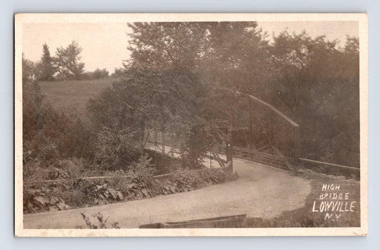 Postcard front showing High Bridge along a curved rural road at Lowville, New York, with timber truss structure partly obscured by trees; divided back, postmarked 1909.
