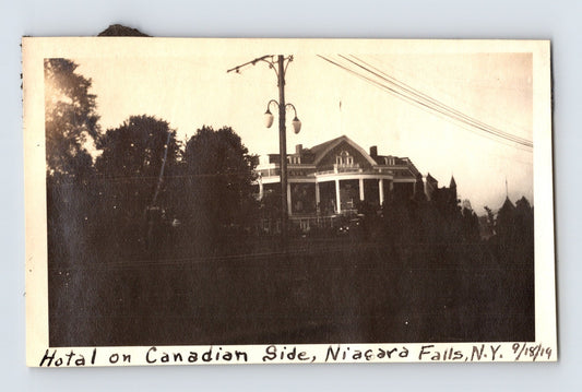 1919 snapshot photo showing a large hotel building on the Canadian side of Niagara Falls, viewed from New York with utility poles and trees in the foreground.