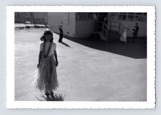 Girl hula costume grass skirt schoolyard children background mid century snapshot