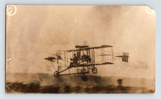 Early Curtiss pusher biplane in flight with tricycle landing gear and exposed framework over open landscape circa 1910s