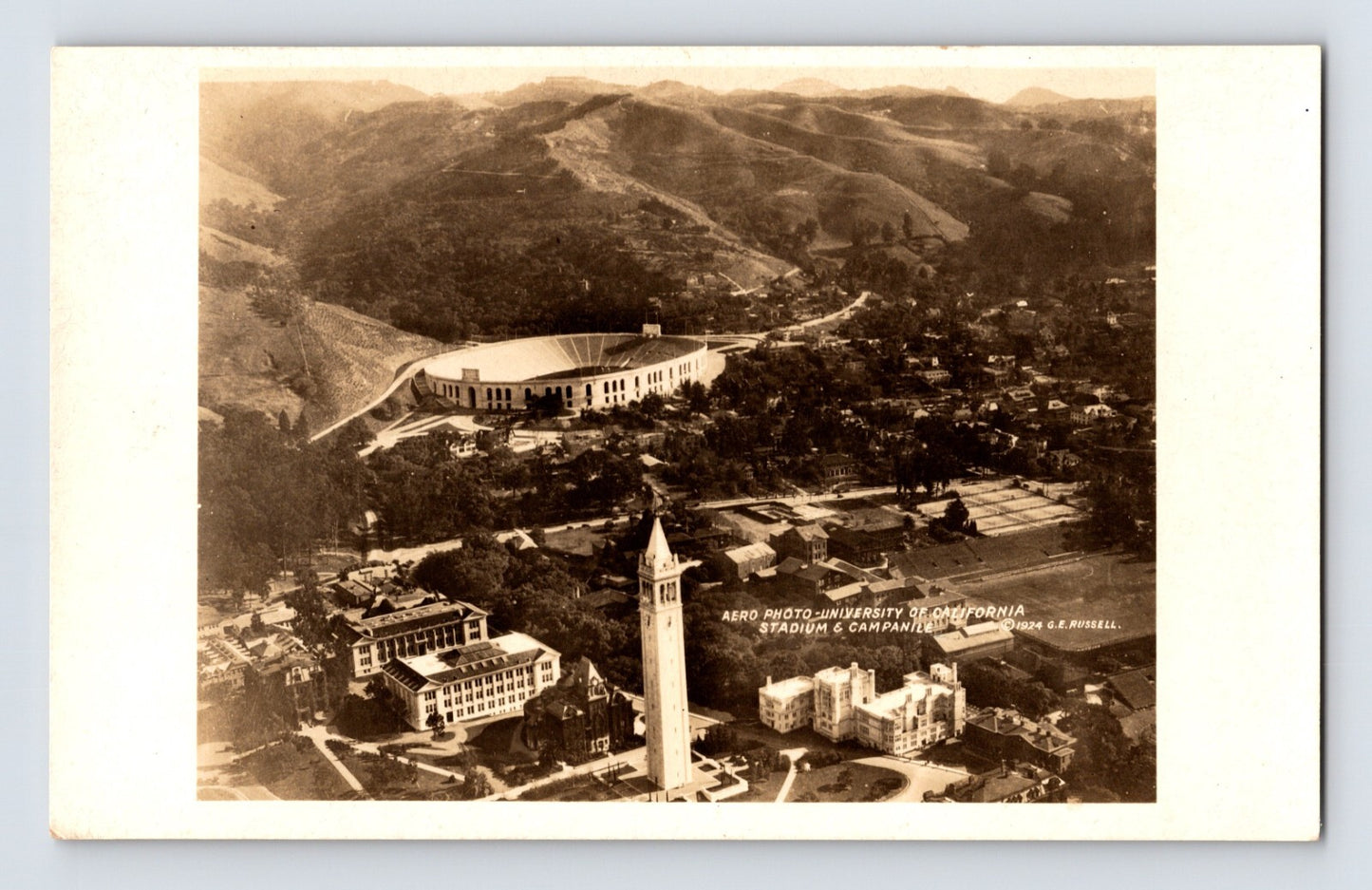 Aerial view of the University of California campus in Berkeley with Sather Tower, California Memorial Stadium, and surrounding hills, 1920s real photo postcard.