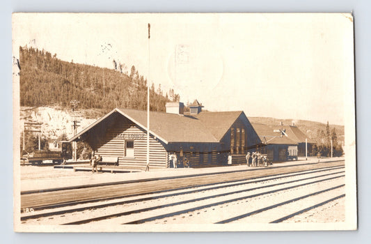1925 real photo postcard showing the railroad station at Lake Louise, British Columbia, with multiple train tracks, log-style depot buildings, and mountain terrain in the background.
