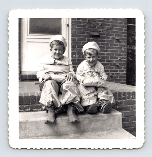 Halloween snapshot two children costume outfits sitting on brick steps pillow stuffing hats mid century home 1950s photo scalloped edge