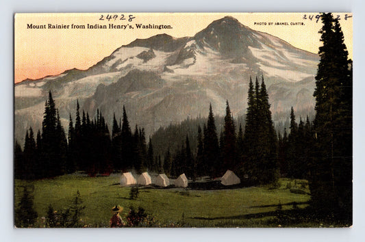 1910s postcard view of Mount Rainier from Indian Henry’s Camp in Washington, featuring snow-covered peaks, evergreen forest, and a row of white canvas tents beneath the mountain at sunset.